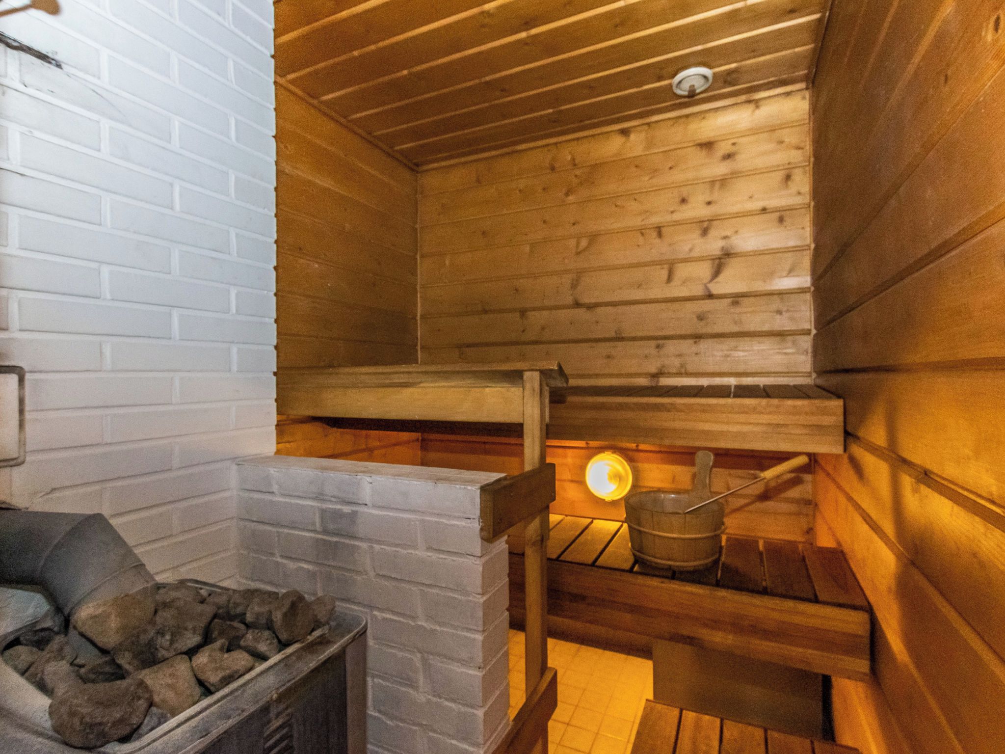 A wooden cabin interior with a stone fireplace, a wooden bench, and a metal bucket.