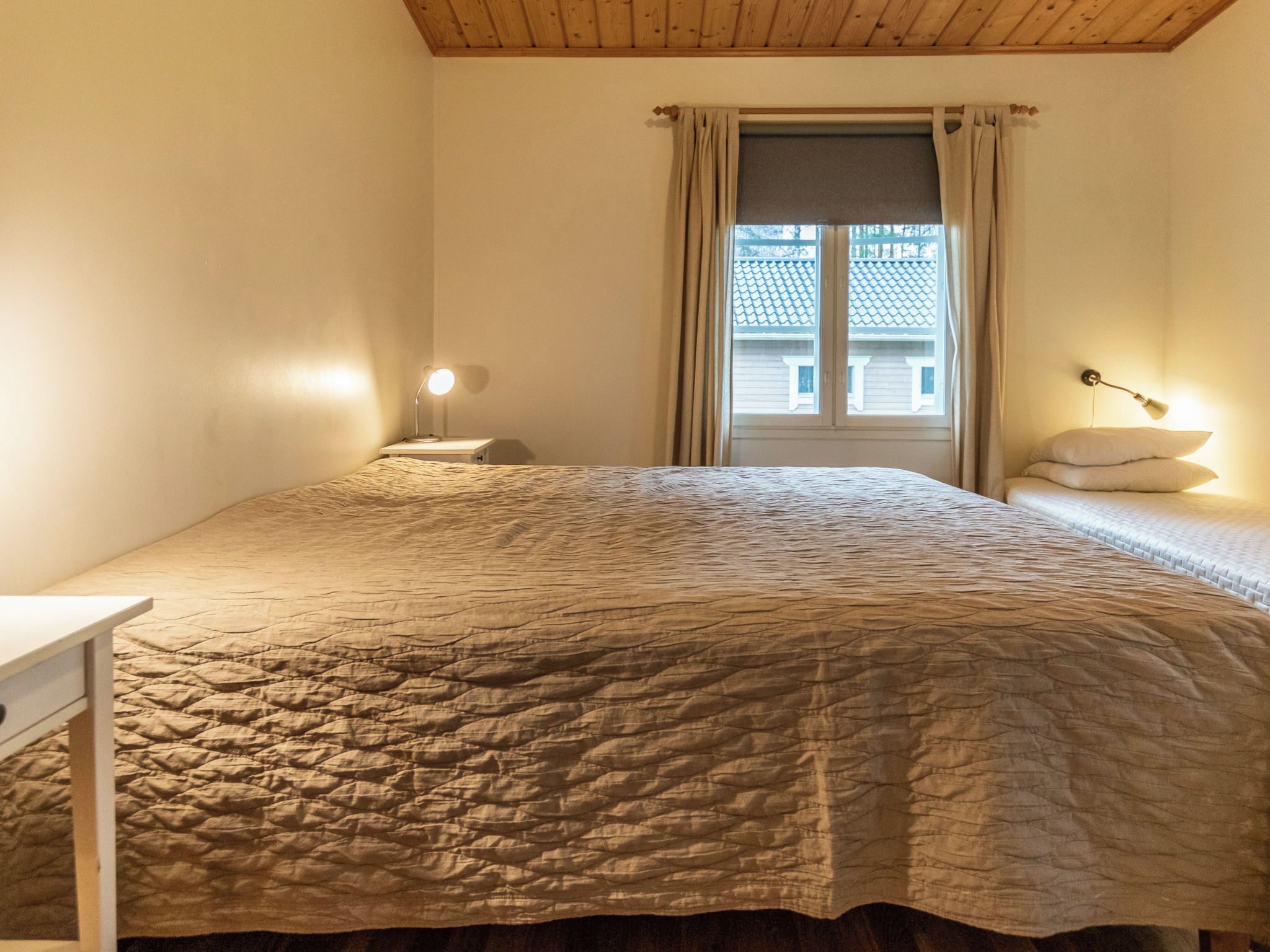 Un dormitorio con cama, mesita de noche, lámpara y ventana con cortinas.