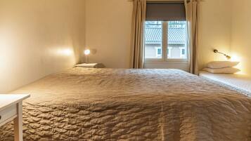 Une chambre à coucher avec un lit, une table de chevet, une lampe et une fenêtre avec des rideaux.
