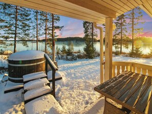 A wooden deck with a bench and a barrel, overlooking a lake with trees and a sunset. - Villa niemi by Interhome (Leppävirta)