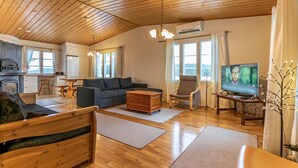 Amplia sala de estar con techo de madera, chimenea, un sofá, un televisor y un comedor.