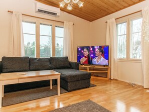 Una sala de estar con un sofá modular, una mesa de centro, un televisor sobre un mueble bajo y ventanas amplias con cortinas.