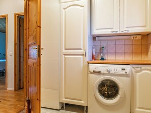 Une buanderie équipée d’un lave-linge à chargement frontal, de meubles en bois et d’un pare-feu en carrelage.