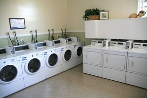 A laundry facility with multiple washing machines and dryers, a notice board, and a shelf with decorative items.