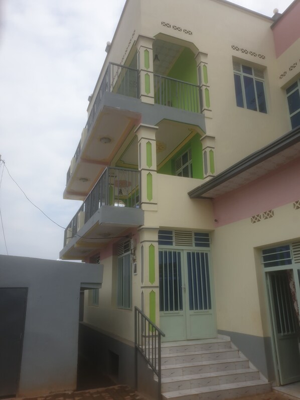 Un immeuble à plusieurs étages doté de balcons, d’un escalier et d’une entrée fermée par un portail.