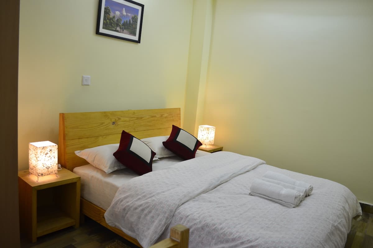 A neatly made bed with white linens and two red and white pillows, flanked by bedside tables with lamps.