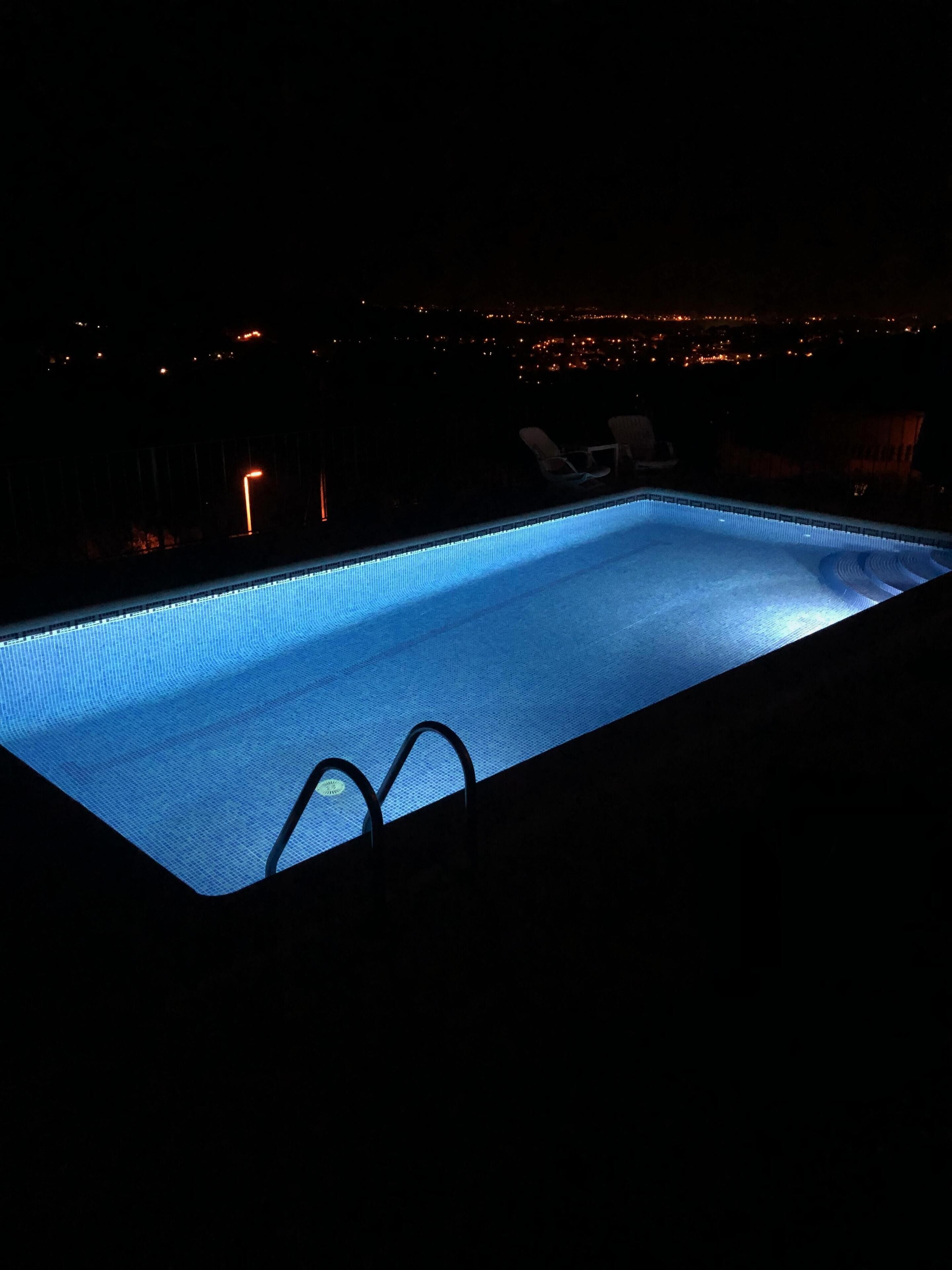 A swimming pool at night with a view of a cityscape in the background.