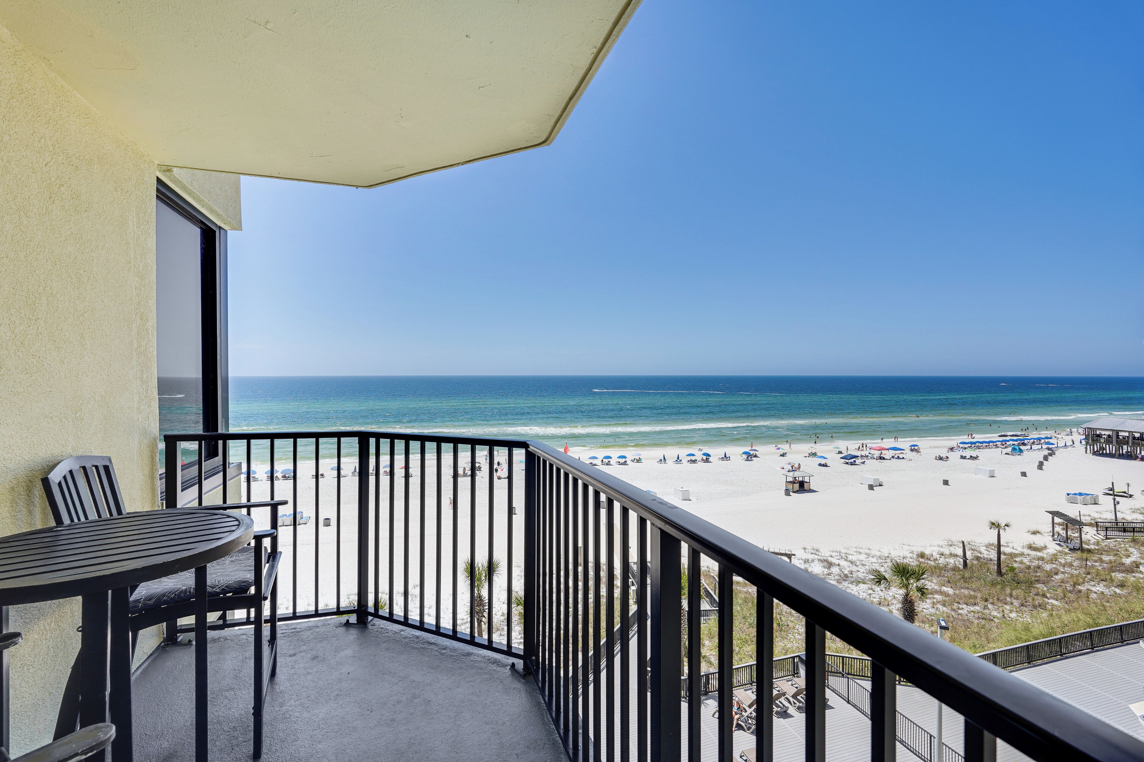 A balcony with a view of a beach, a table, and chairs.