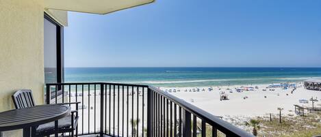A balcony with a view of a beach, a table, and chairs.