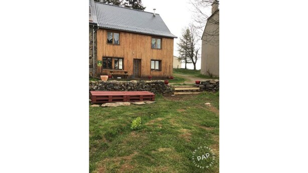 A wooden house with a stone foundation, a stone wall, and a wooden bench.