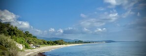 Eine Küstenlandschaft mit Strand, blauem Himmel und fernen Bergen.
