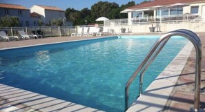 Ein Pool mit einer Metallleiter, umgeben von Liegestühlen und einem weißen Zaun.