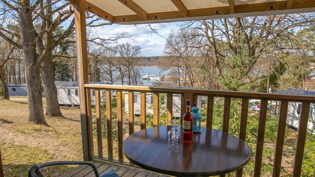 A wooden deck with a round table, chairs, and a view of a lake and boats.