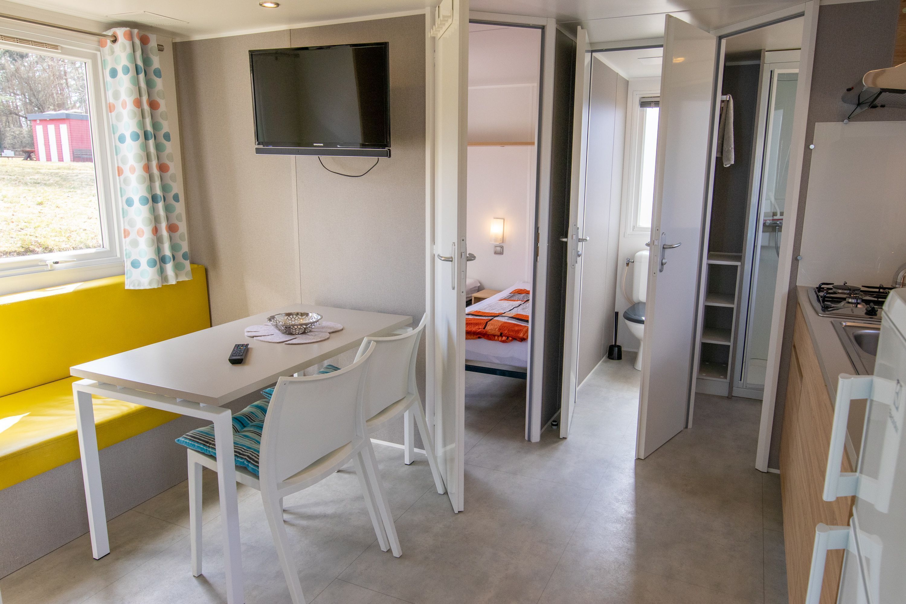 A compact room with a bed, a small table with chairs, a television, and a window with curtains.