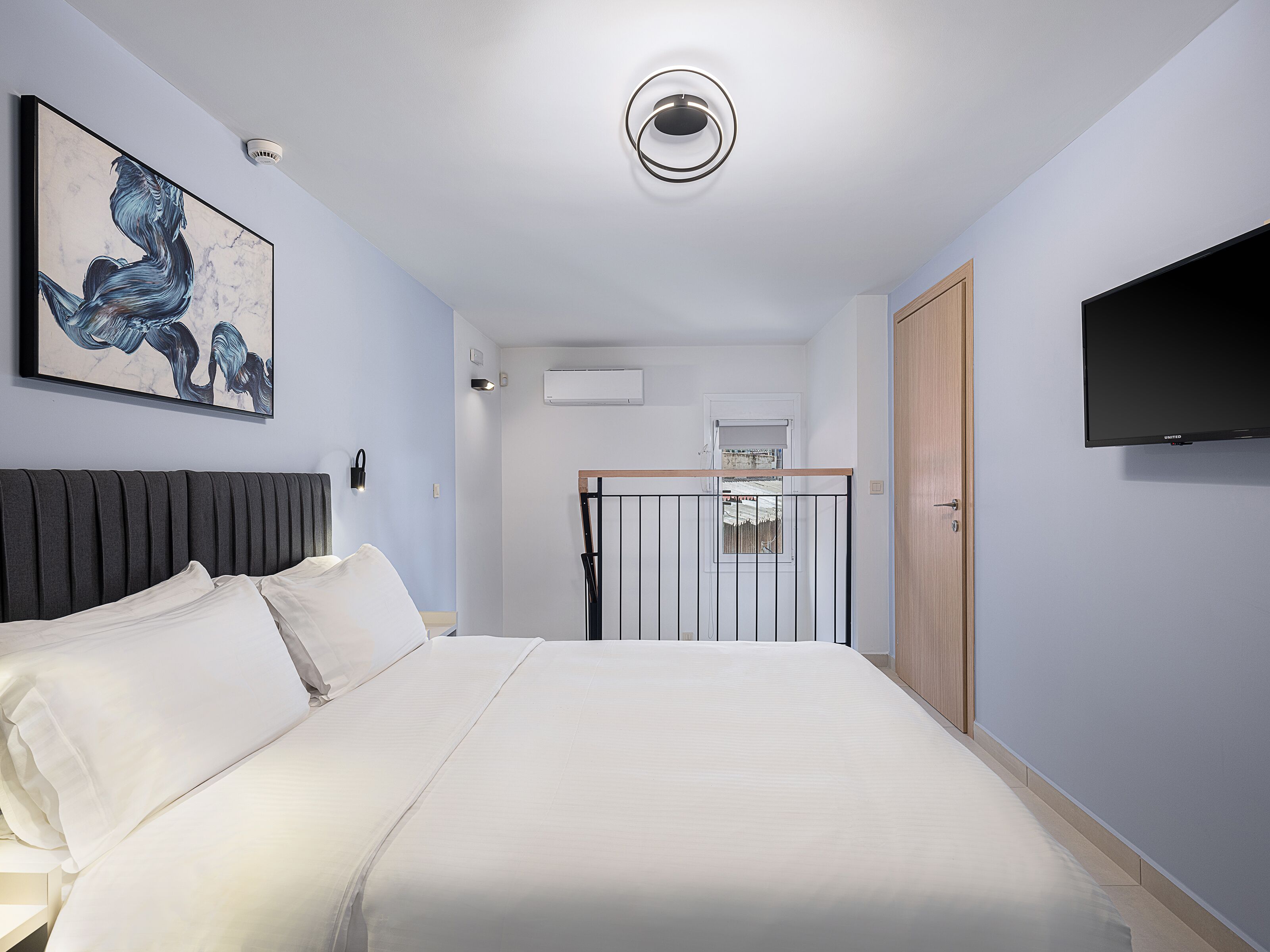 A modern bedroom with a large bed, a mounted TV, and a painting on the wall.
