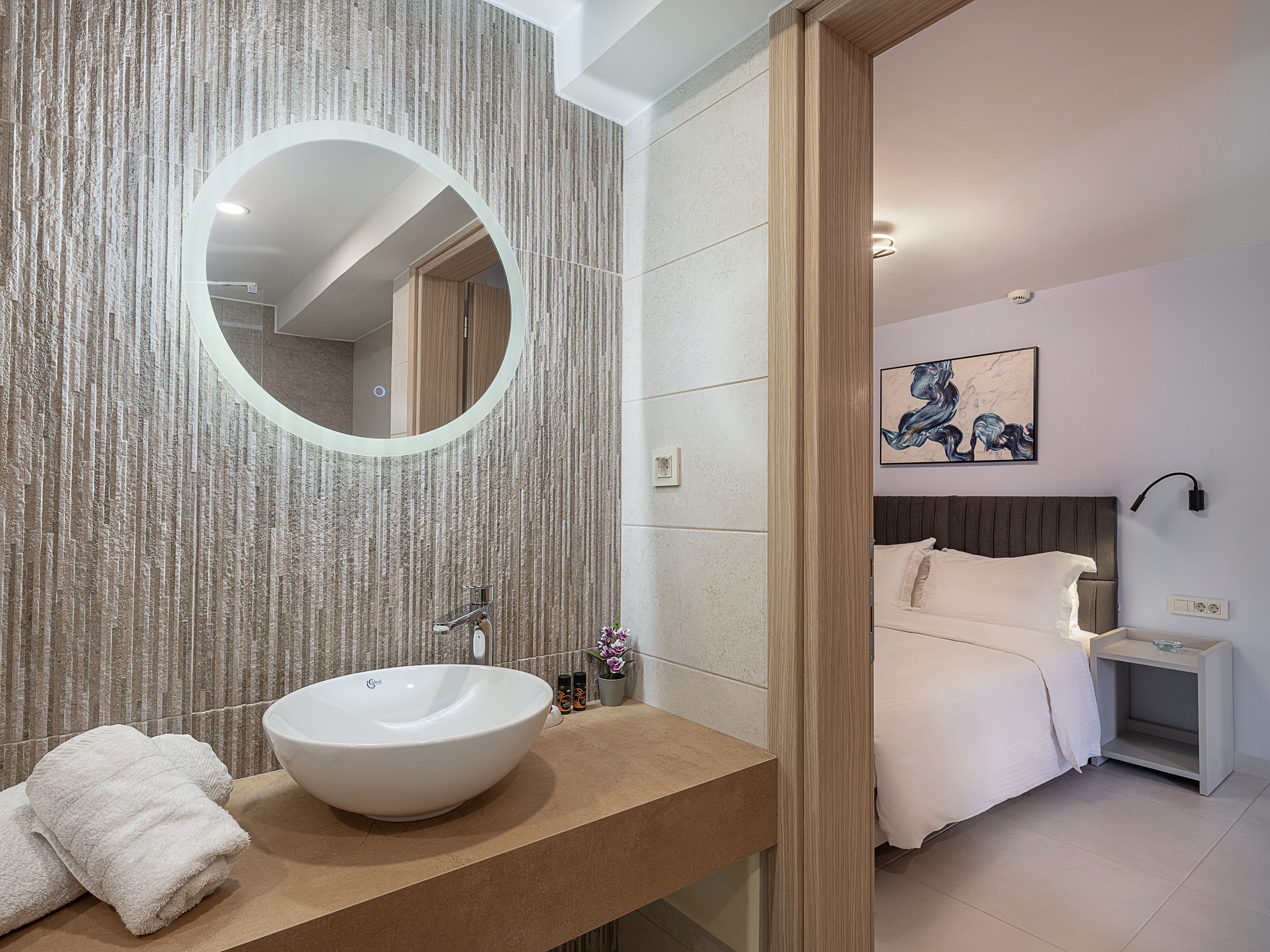 A modern bathroom with a large round mirror, a white sink, and a towel on the counter.