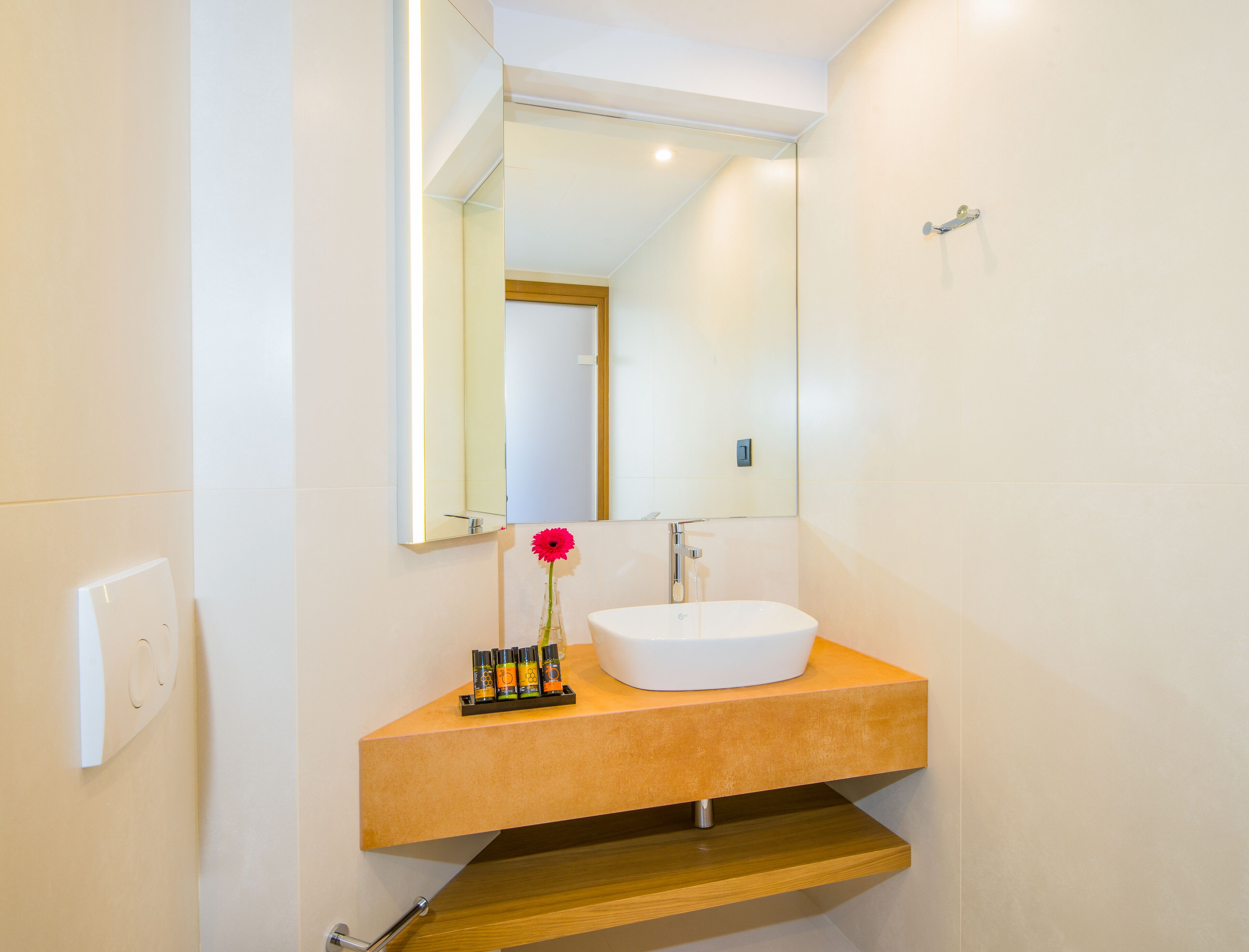 A modern bathroom with a white sink, a mirror, and a wooden shelf.