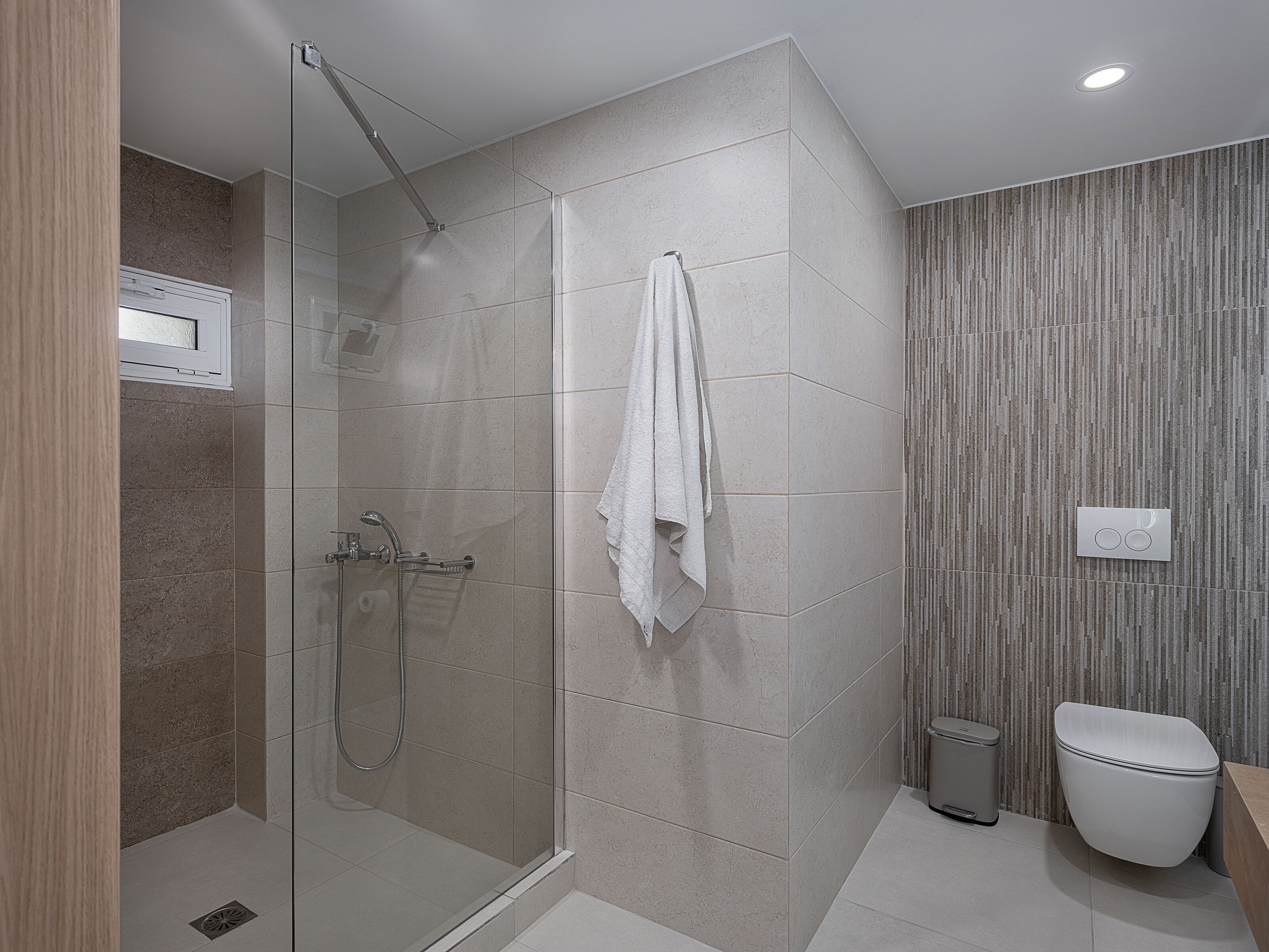 A modern bathroom with a glass-enclosed shower, a white toilet, and a towel hanging on the wall.