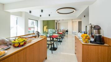 Une cuisine d’hôtel moderne dotée d’un espace buffet, d’un coin repas avec tables et chaises, et d’un espace dédié aux boissons chaudes.