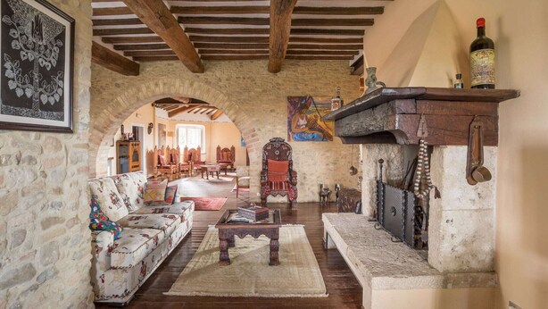 Una sala de estar rústica con paredes de piedra, vigas de madera, chimenea y muebles tradicionales.