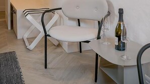 Una habitación moderna con una silla blanca, una mesita con una botella y vasos, y una lámpara colgante.