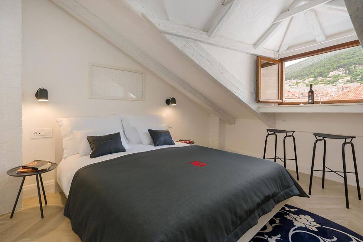 Un dormitorio con una cama grande, un tragaluz, una ventana con vistas y dos taburetes de bar.