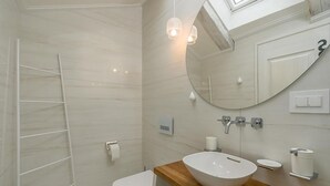 Un baño moderno con un espejo grande, un tocador de madera, un lavabo blanco y una zona de ducha con una escalera.
