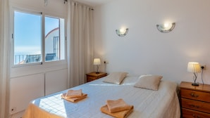 Ein Hotelzimmer mit Bett, zwei Nachttischen mit Lampen, einem Fenster mit Vorhängen und Blick ins Freie.