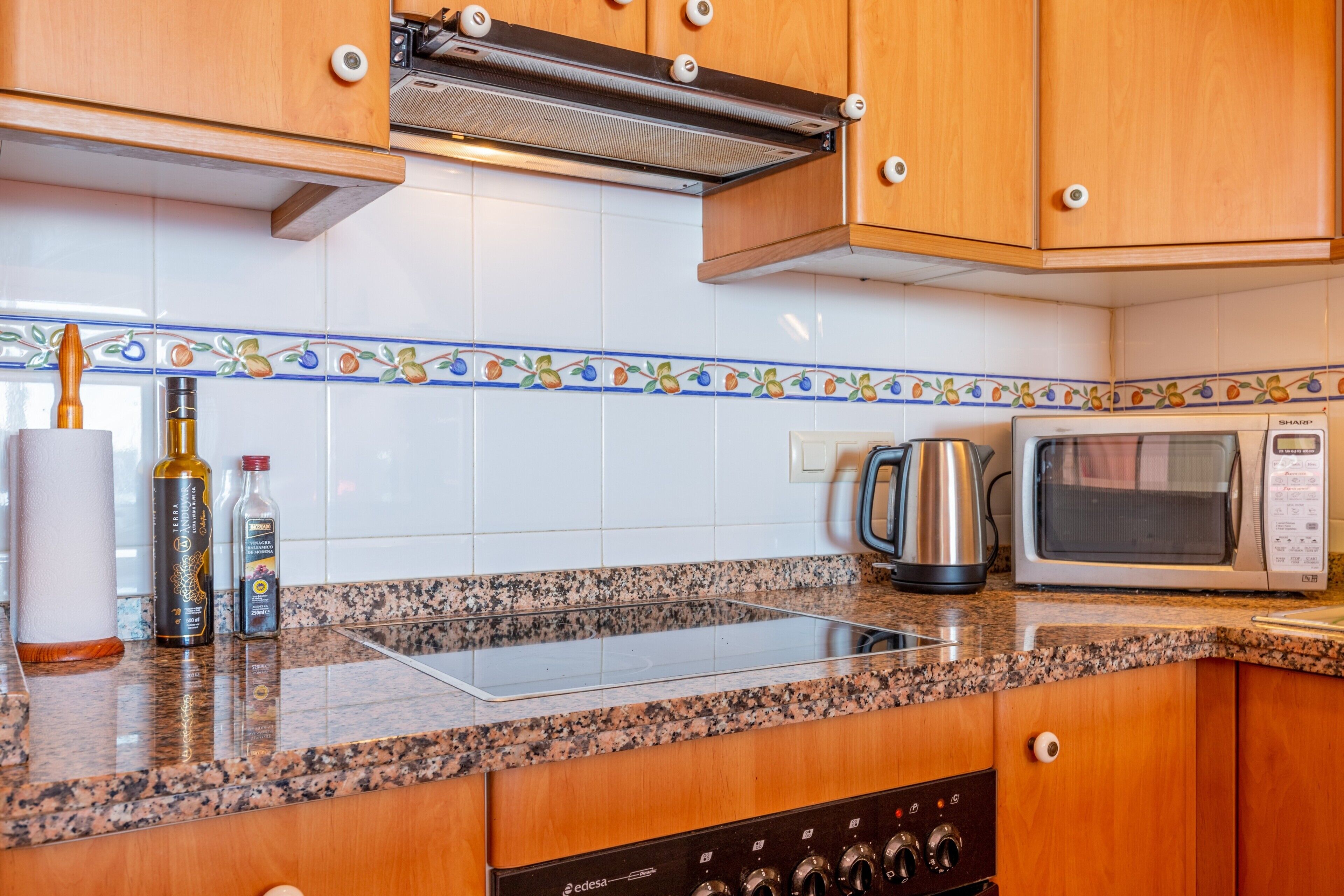 A kitchen with wooden cabinets, a microwave, a kettle, and a stove.