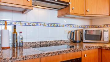 A kitchen with wooden cabinets, a microwave, a kettle, and a stove.