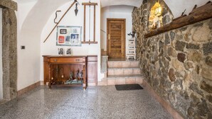 Un pasillo de paredes de piedra con una escalera de madera, un escritorio con teléfono y una lámpara fijada a la pared.