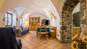 Un interior con comedor, cocina y sala de estar, destacando arcos de piedra y suelo de baldosas.