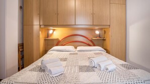 A neatly made bed with pillows and rolled towels, wooden headboard, and bedside lamps. - Apartment "Bellavista" with Lake Views & Terrace (Mezzolago)