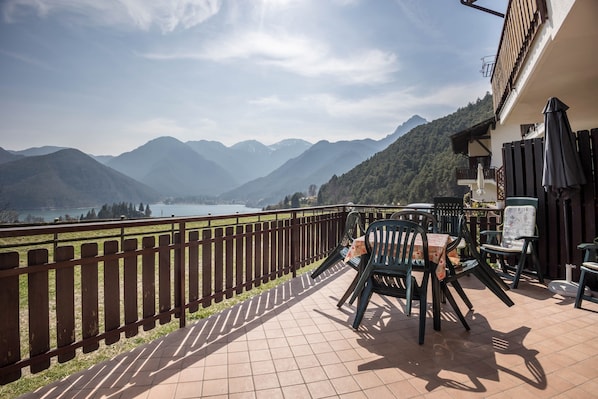 Una terraza con vistas a montañas y un lago, mobiliario exterior y una valla de madera.