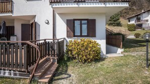 A two-story building with a wooden balcony, a small garden with yellow flowers, and a staircase leading to the entrance. - Apartment "Bellavista" with Lake Views & Terrace (Mezzolago)