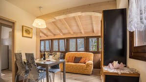 Una sala de estar acogedora con techo de madera, un sofá, una mesa de comedor con sillas y vistas amplias a través de grandes ventanas.