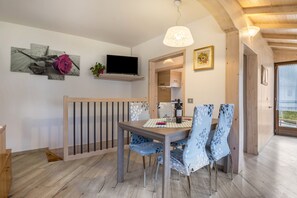 A dining area with a wooden table, chairs, a TV, and a hanging light fixture.