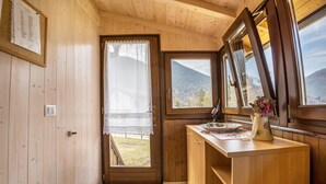 Un interior de madera con una puerta que da a un área exterior, una ventana con vistas a montañas y una encimera con un florero.