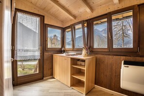 A wooden cabin interior with a kitchen area, large windows with mountain views, and a wooden ceiling.
