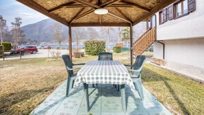 Un espacio de estar al aire libre techado, con una mesa y sillas, techo de madera y vistas a una montaña y un lago.