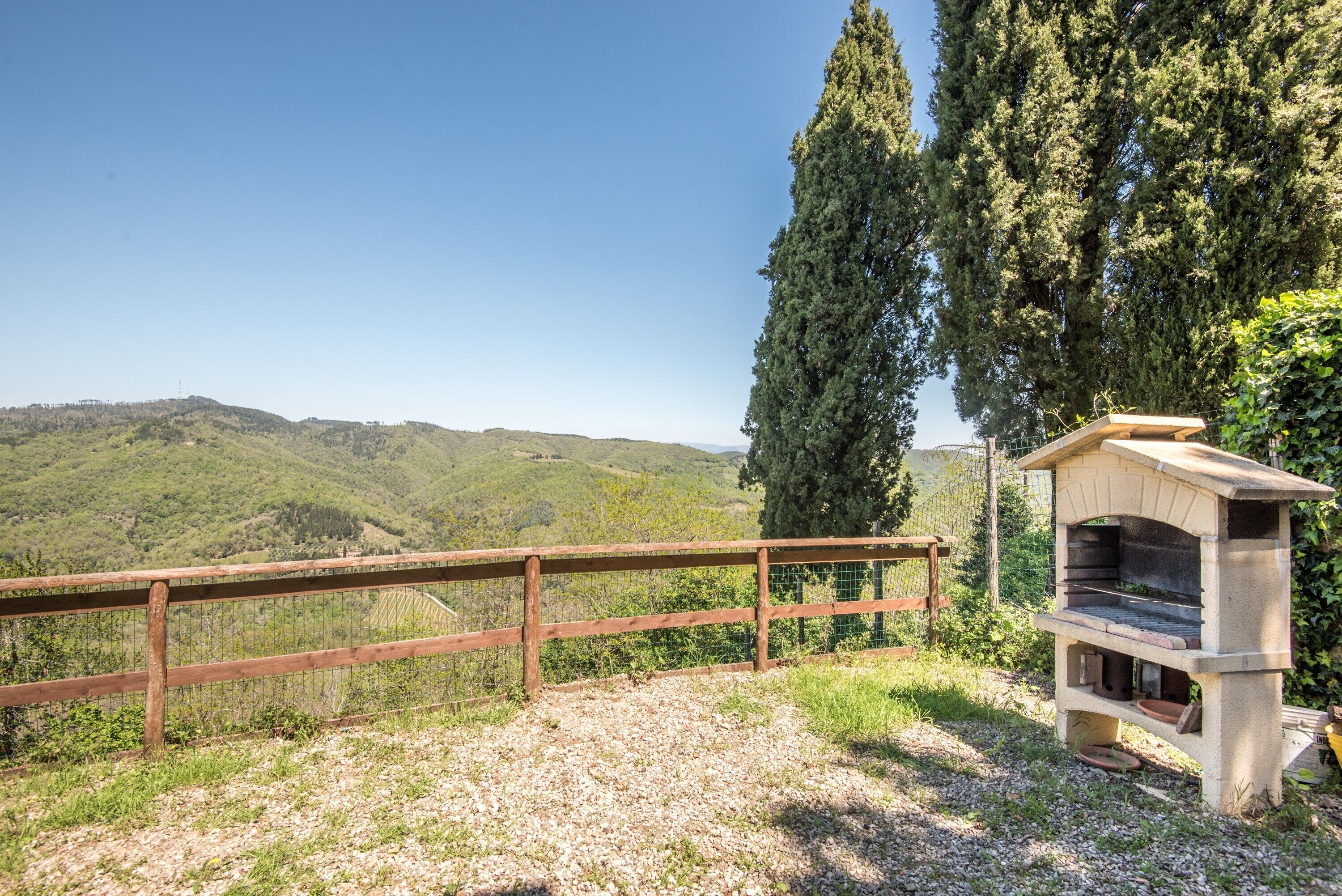 Un ambiente rustico all'aperto con un recinto in legno, un forno in pietra e vista su dolci colline.