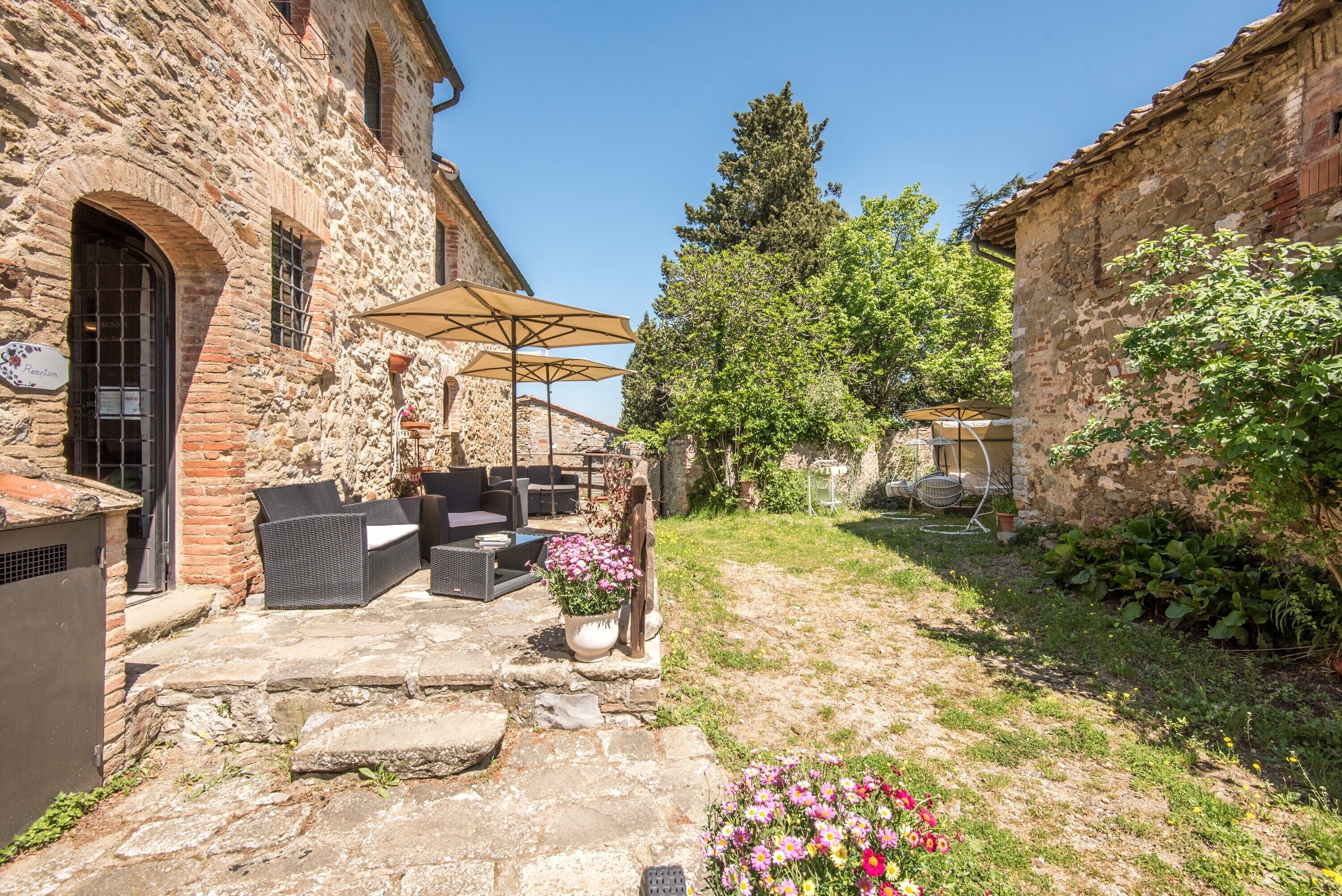 Un bâtiment en pierre doté d’un patio aménagé avec du mobilier d’extérieur et des parasols, le tout entouré de verdure.