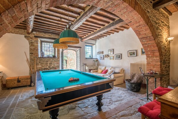 A billiards table in a room with stone walls, a wooden ceiling, and a cozy seating area.