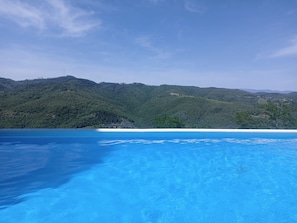 Una piscina cristallina con vista su colline verdi e un edificio in lontananza.