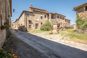 Un edificio in pietra con una strada pavimentata, un piccolo giardino e un cartello che indica un ristorante.