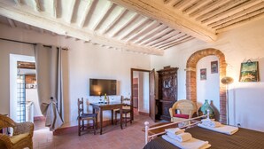 A room with a bed, a desk, a chair, a television, and a large arched doorway. - Casale Rosennano Apartment – Shared Garden, Wi-Fi, Medieval Setting (Rosennano)