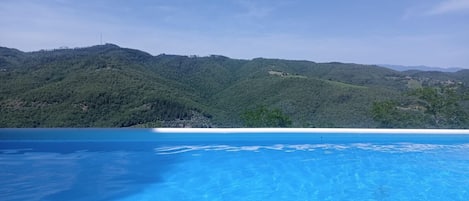 A clear blue pool with a view of green hills and a distant building.