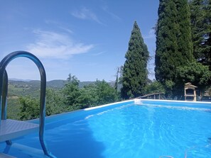 A clear blue swimming pool with a metal ladder, surrounded by lush greenery and tall trees, overlooking a hilly landscape. - Casale Rosennano Apartment – Shared Garden, Wi-Fi, Medieval Setting (Rosennano)