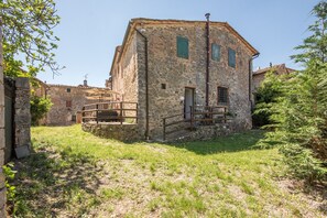 Un bâtiment en pierre avec un escalier en bois menant à une porte, le tout entouré de verdure.