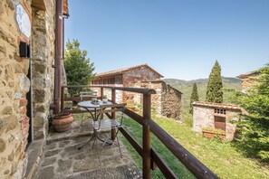A stone building with a wooden balcony, a table with chairs, and a potted plant. - Casale Rosennano Apartment – Shared Garden, Wi-Fi, Medieval Setting (Rosennano)